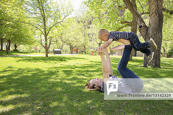 Side view of playful mother balancing son on legs at park