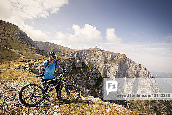 Male cyclist looking away while standing with bicycle on mountain