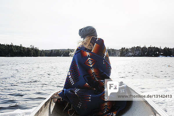Rückansicht einer Frau mit Decke  die im Winter im Algonquin-Provinzpark im Boot auf dem See sitzt