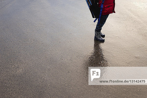 Niedriger Teil eines Jungen mit Rucksack auf nasser Straße stehend