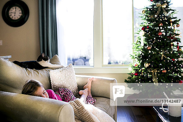 Mädchen schläft zu Hause auf dem Sofa am Weihnachtsbaum
