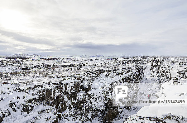 Distant view of father and daughter amidst snow covered rock formations against sky