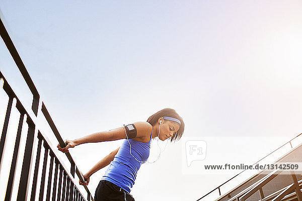 Seitenansicht einer Frau  die sich auf einem Geländer gegen den klaren Himmel streckt
