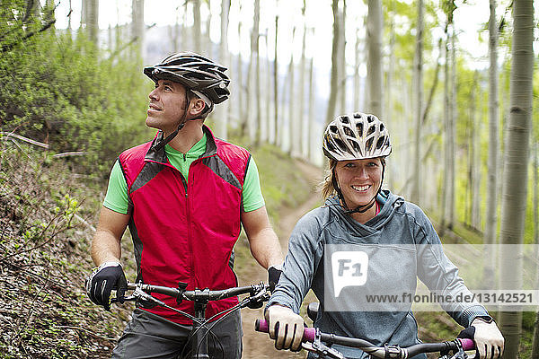 Porträt einer Radfahrerin  die im Wald bei einem Freund mit Fahrrad steht
