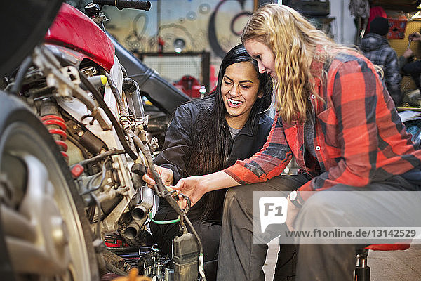 Happy female mechanics repairing bike in workshop