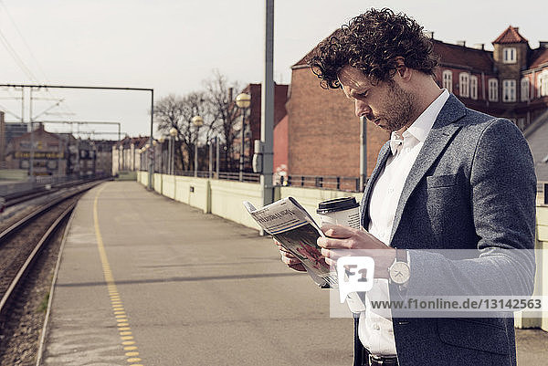 Businessman reading newspaper while standing on railroad station platform