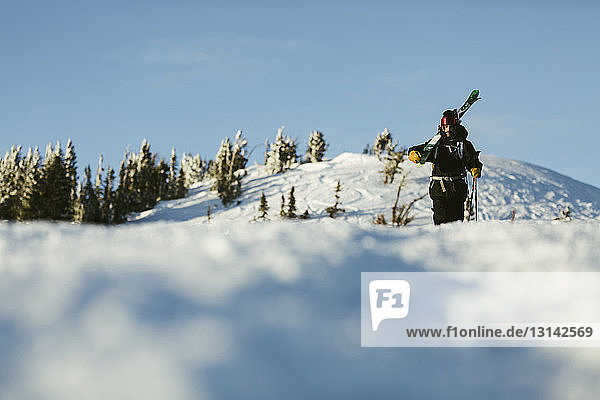 Surface level image of man with skies walking on snow covered mountain against sky