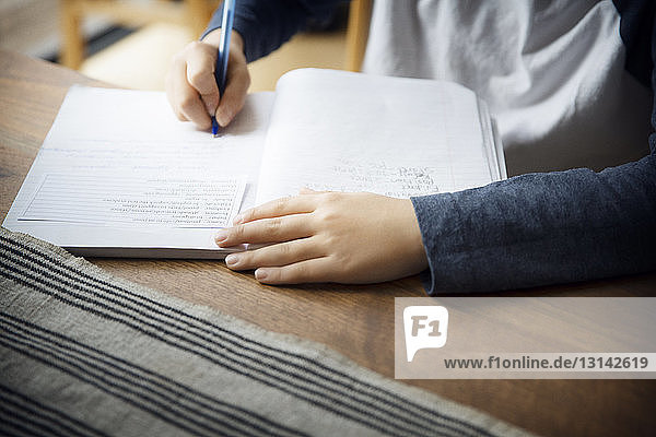 Midsection of boy writing in book on table at home