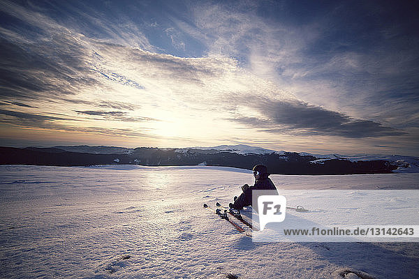 Skifahrer  der auf schneebedecktem Berg sitzend gegen den Himmel blickt
