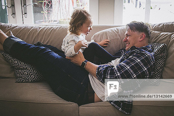 Father playing with girl on sofa at home