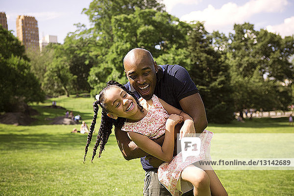 Happy father and daughter enjoying on grassy field at park