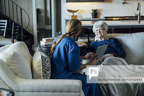 Hausangestellte diskutiert über Tablet-Computer mit älterer Frau im Wohnzimmer