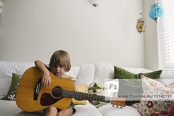 Mädchen spielt Gitarre  während sie zu Hause auf dem Sofa sitzt