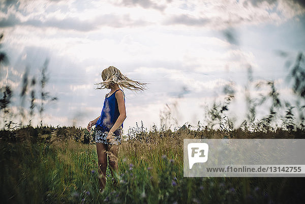 Mädchen wirft Haare  während sie auf dem Feld gegen den Himmel steht