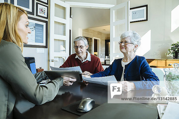 Älteres Ehepaar hält Dokumente in der Hand  während es mit dem amtierenden Finanzberater diskutiert