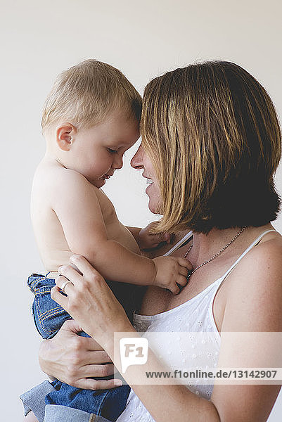 Mother and shirtless son touching foreheads against white background
