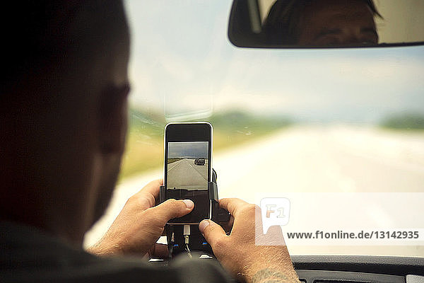 Mann benutzt Mobiltelefon  während er mit einem Freund im Auto sitzt