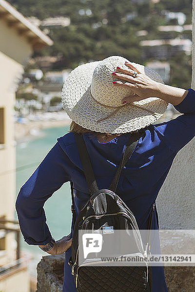 Rückansicht einer im Dorf stehenden Touristin mit Rucksack und Hut