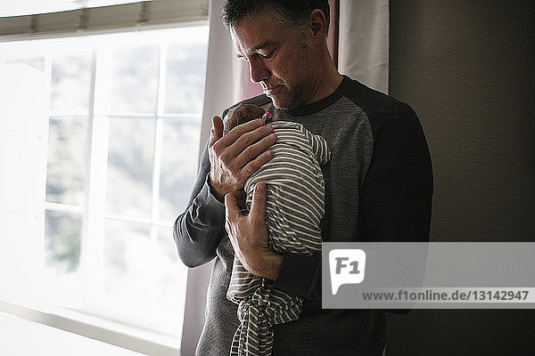 Father carrying newborn daughter while standing at home