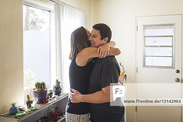 Side view of couple embracing by window at home