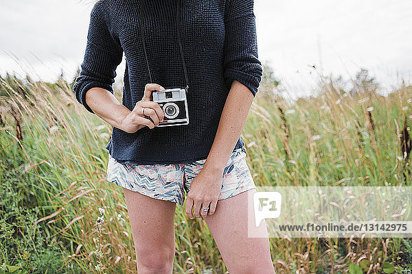 Midsection of woman holding instant camera while standing on grassy field