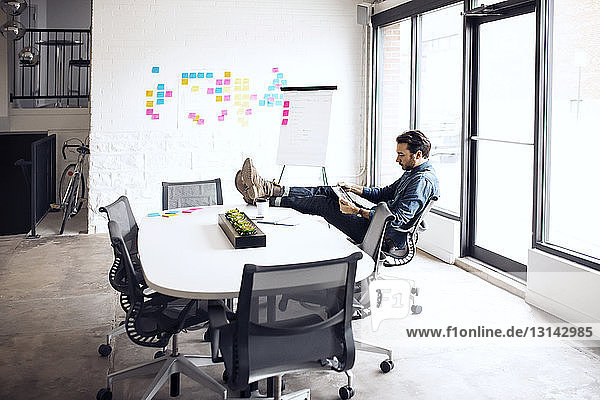 Geschäftsmann benutzt Tablet  während er im Kreativbüro auf einem Stuhl sitzt