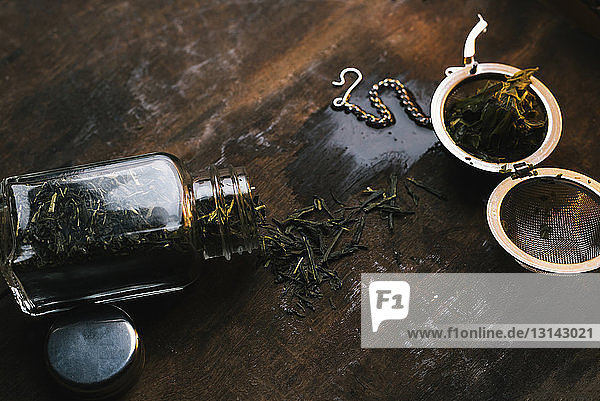 Nahaufnahme eines Teesiebs mit getrockneten Blättern in einem Glas auf einem Holztisch