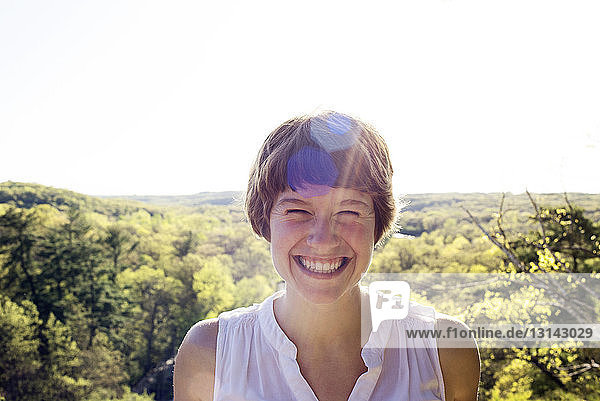 Portrait of cheerful woman against trees on sunny day
