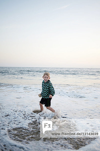 Lächelnder Junge spielt am Ufer am Strand gegen den Himmel