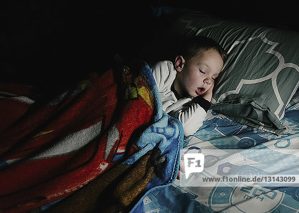 Hochwinkelaufnahme eines Jungen  der zu Hause in der Dunkelkammer auf einem Bett schläft
