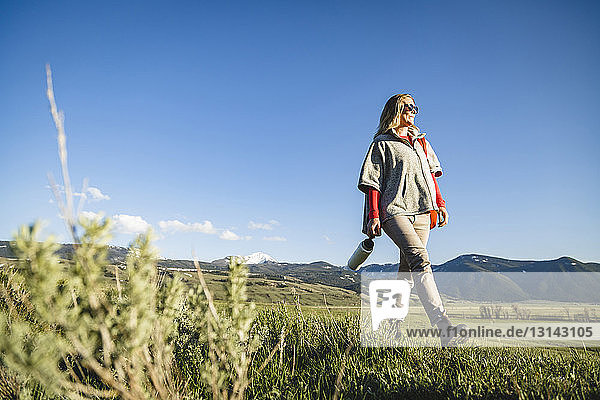 Low angle view of female hiker walking on field against sky