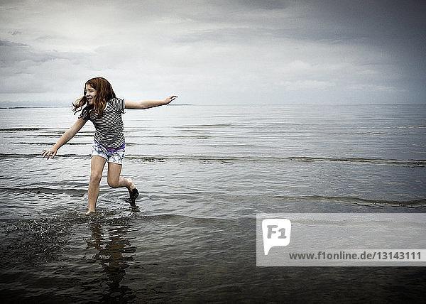 Happy girl running on sea shore against cloudy sky