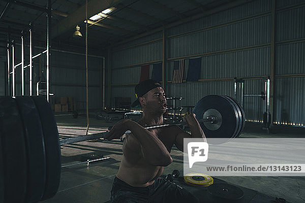 Männlicher Athlet ohne Hemd beim Langhantelheben im Fitnessstudio