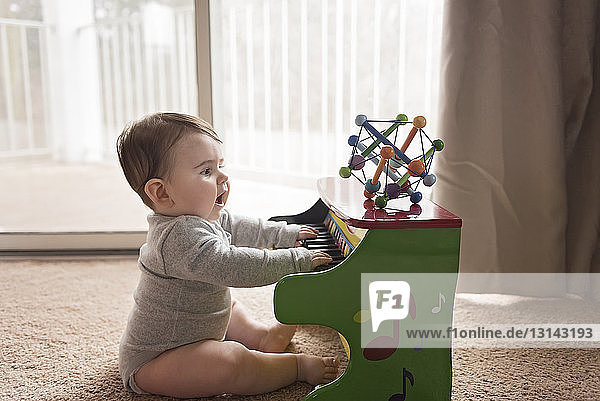 Seitenansicht eines neugierigen kleinen Jungen  der zu Hause Spielzeugklavier spielt