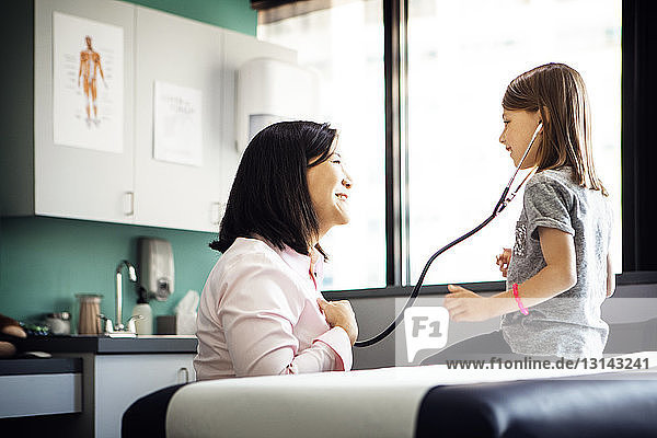 Seitenansicht eines Mädchens  das den Herzschlag einer Ärztin durch ein Stethoskop in der Klinik hört