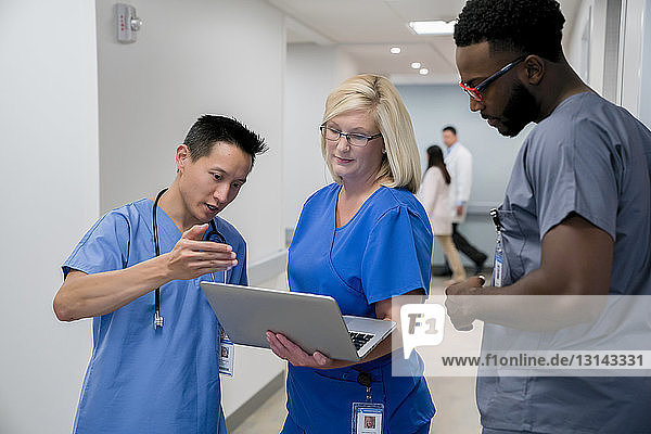 Arzt diskutiert mit Kollegen über Laptop-Computer  während er im Krankenhauskorridor steht