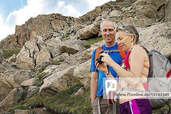 Happy couple looking at digital camera while standing by mountain