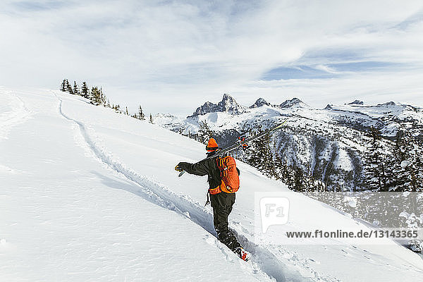 Wanderer trägt Ski auf der Schulter  während er einen schneebedeckten Berg besteigt