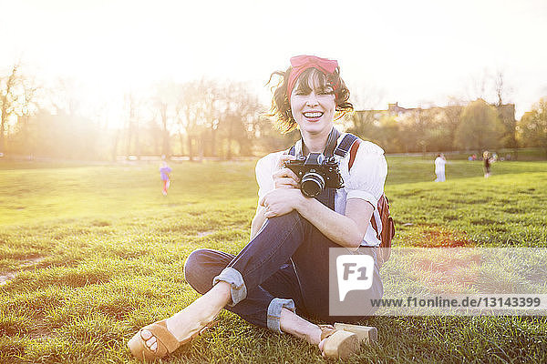 Portrait of happy woman with camera sitting in park