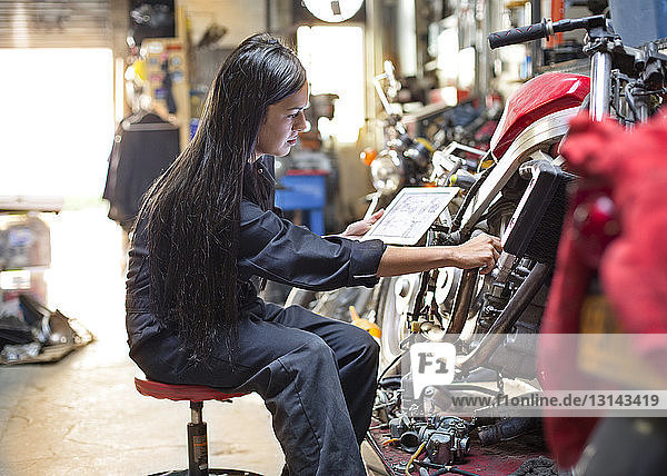Side view of woman holding digital tablet while repairing bike in workshop