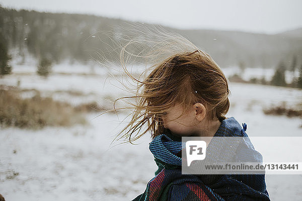 Girl wrapped in blanket standing on snowy field