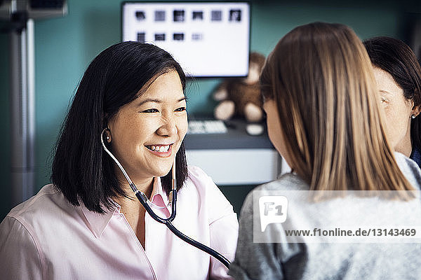 Happy female doctor examining girl with stethoscope in clinic