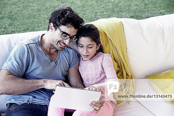 Lächelnder Vater und lächelnde Tochter benutzen digitales Tablet  während sie auf dem Sofa sitzen