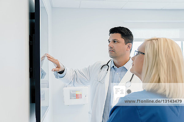 Arzt zeigt auf Flachbildschirm  während er mit einer Kollegin im Krankenhaus diskutiert