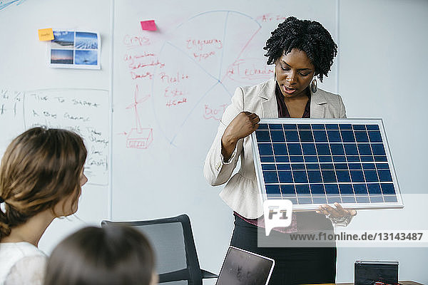 Businesswoman explaining solar panel model during meeting in office