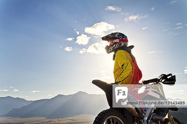 Biker looking at mountains while standing by dirt bike against sky