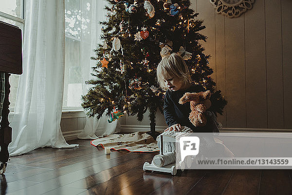 Mädchen spielt zu Hause mit Spielzeug gegen den Weihnachtsbaum