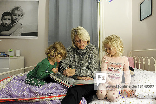 Großmutter erzählt Enkelinnen eine Geschichte  während sie zu Hause auf dem Bett sitzt