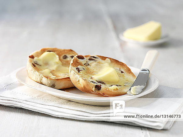 Melting butter on toasted raisin muffin  on plate with butter knife
