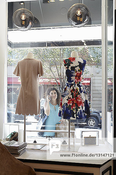 Mature woman  using smartphone  looking in window of fashion boutique